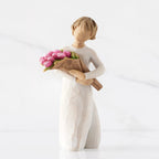Front view of standing figure in cream dress holding bouquet of pink tulips