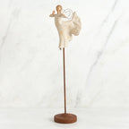 Far shot of angel figurine dressed in white dress dancing with arms and legs out - she is on a brown wooden stand