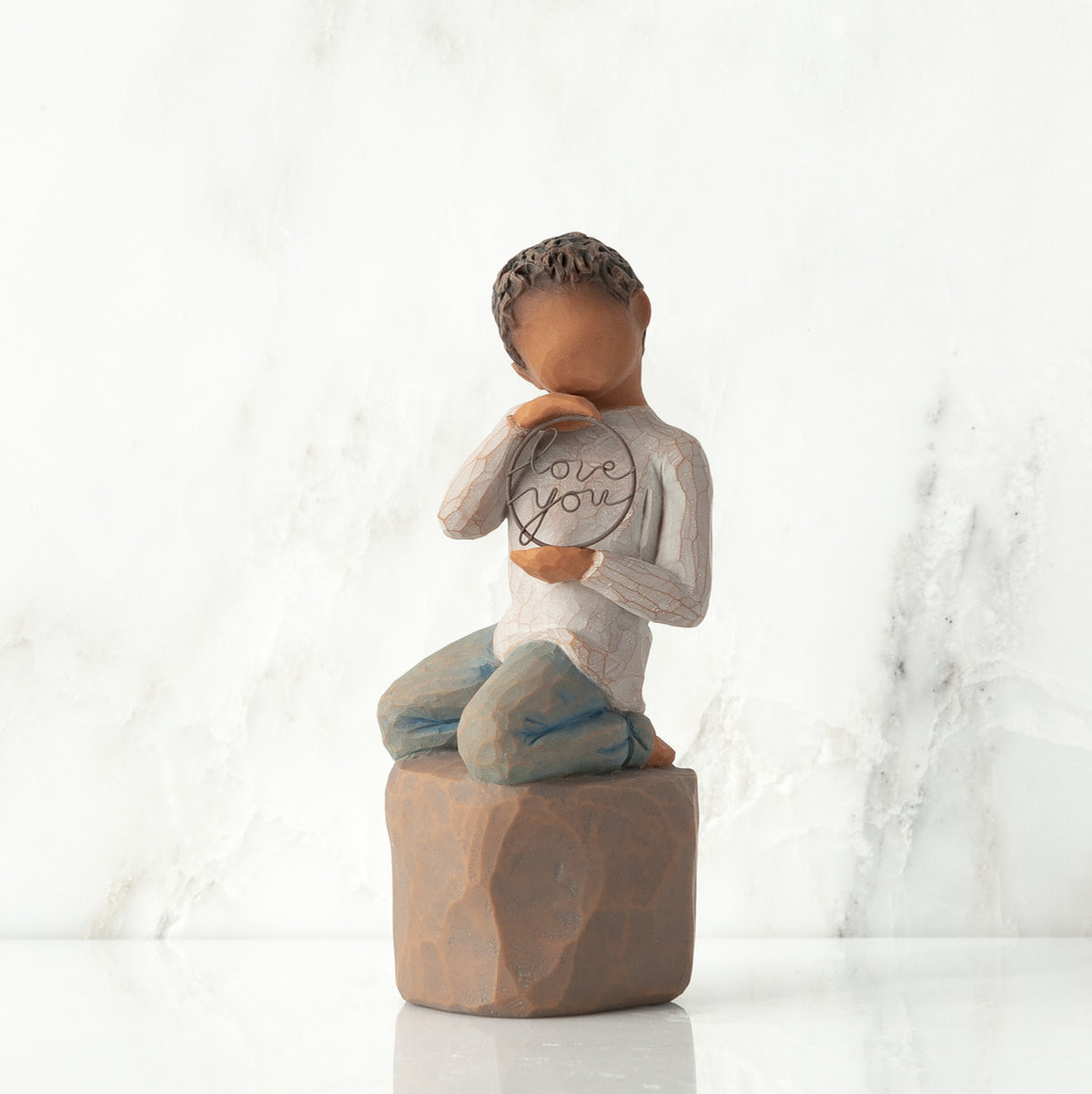 Front view: Figure of darker-skin child, kneeling on rock, holding wire circle with ‘love you’ written in wire