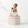 Front: cream square resin box with lid, 3-D figure of seated girl holding cat atop lid