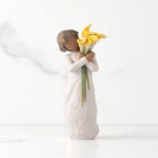 Front view of standing figure in cream dress with darker skin holding yellow calla lilies in her arms