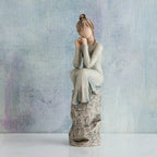 Willow Tree Patience, 7”h hand-painted resin figure in blue/gray dress, hands under chin, sitting on grey rock etched with symbols, in front of muted blue painting