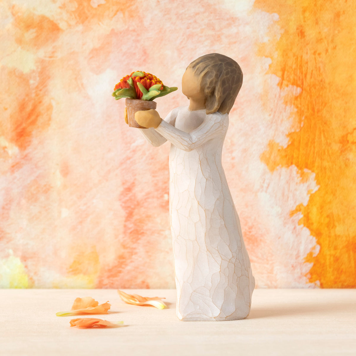 Willow Tree Little Things, 5.25”h hand-painted standing resin figure in cream dress, holding out terracotta pot with orange flowers, in front of orange painting
