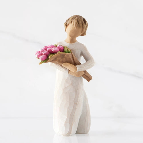 Front view of standing figure in cream dress holding bouquet of pink tulips