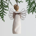 Back view of angel ornament with brown hair in high pony tail leaning forward and holding a red apple up to her face with both hands. Brown string attached to top of angel ornament