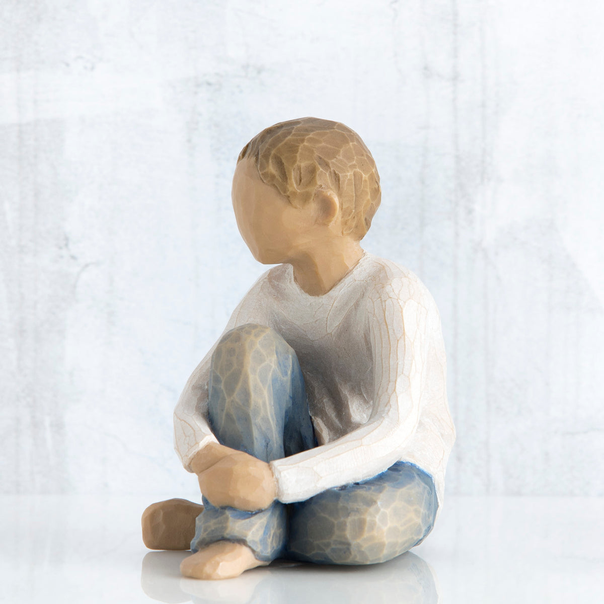 Young brunette boy sitting in white shirt and blue jeans facing close to the front - white background