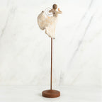 Back view of brunette angel figurine in white dress with arms up, standing on large wooden stand