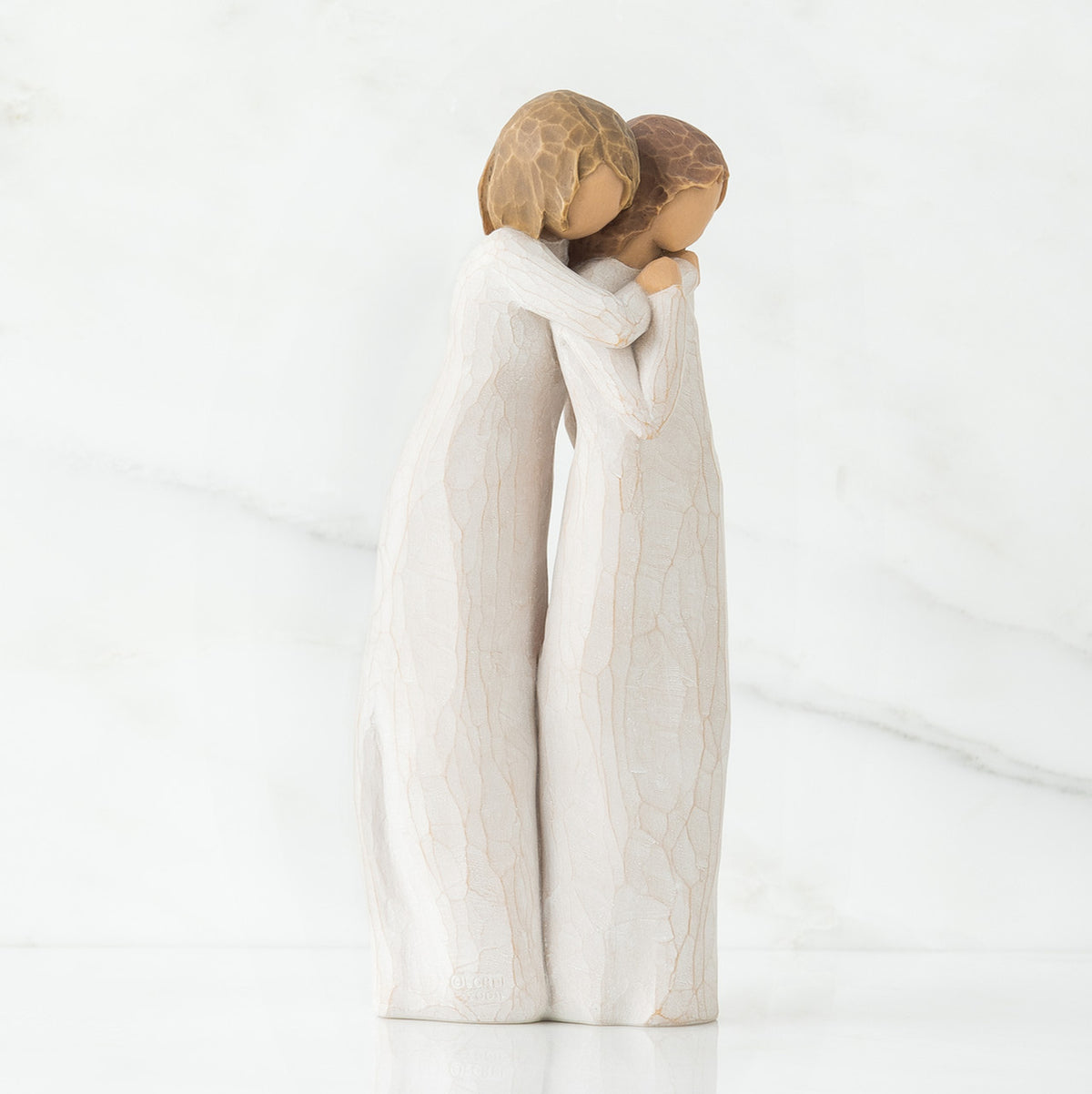 Two woman figurines in white dresses hugging one another facing the side