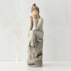 Brunette girl figurine in grey dress sitting on grey rock with her hands to her face