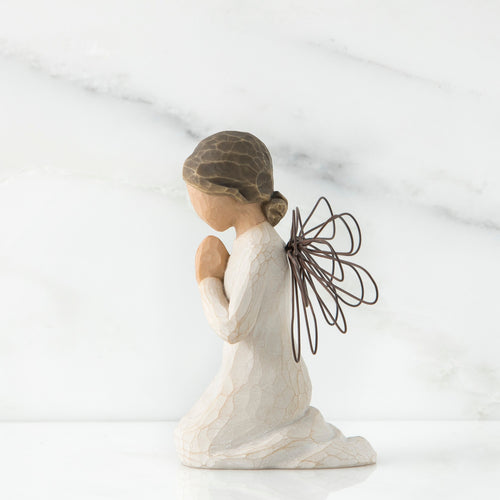 Side view of angel figurine in white kneeling holding her hands in prayer