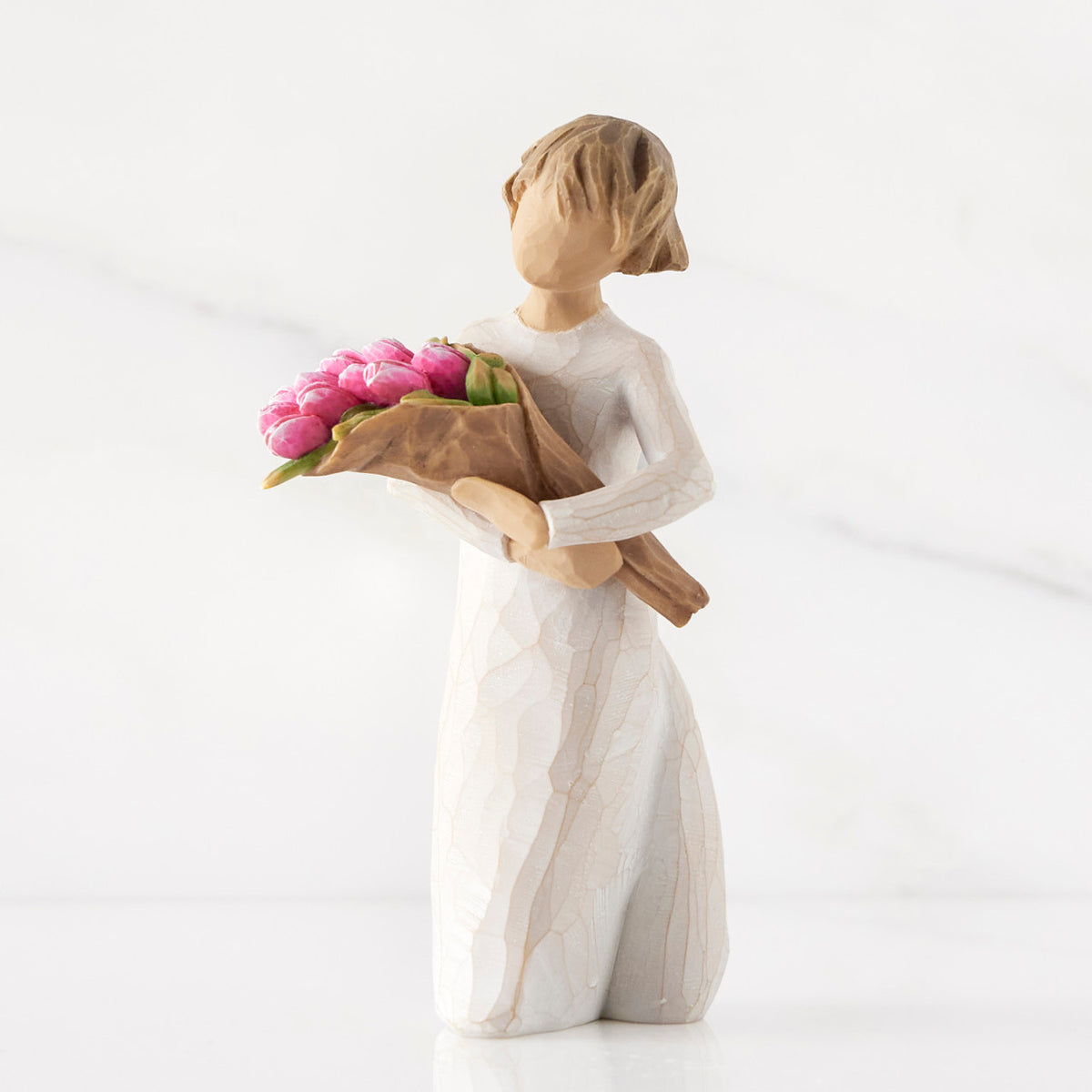 Left side of standing figure in cream dress holding bouquet of pink tulips