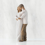 Left view of couple, standing with arms around each other. Woman and man have darker skin tones and hair color.