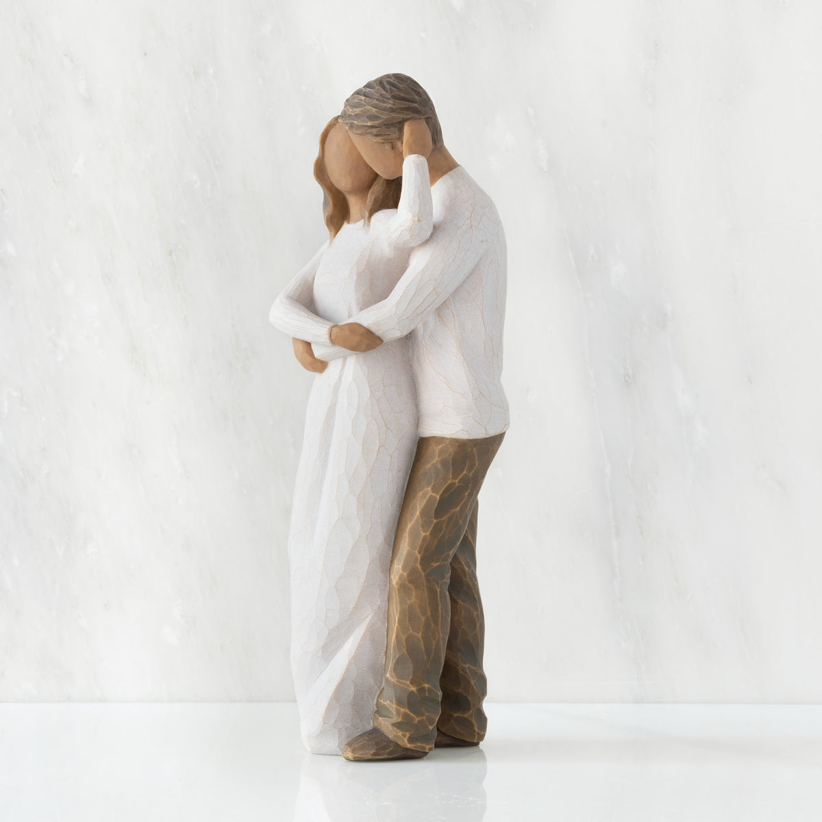 Left view of couple, standing with arms around each other. Woman and man have darker skin tones and hair color.