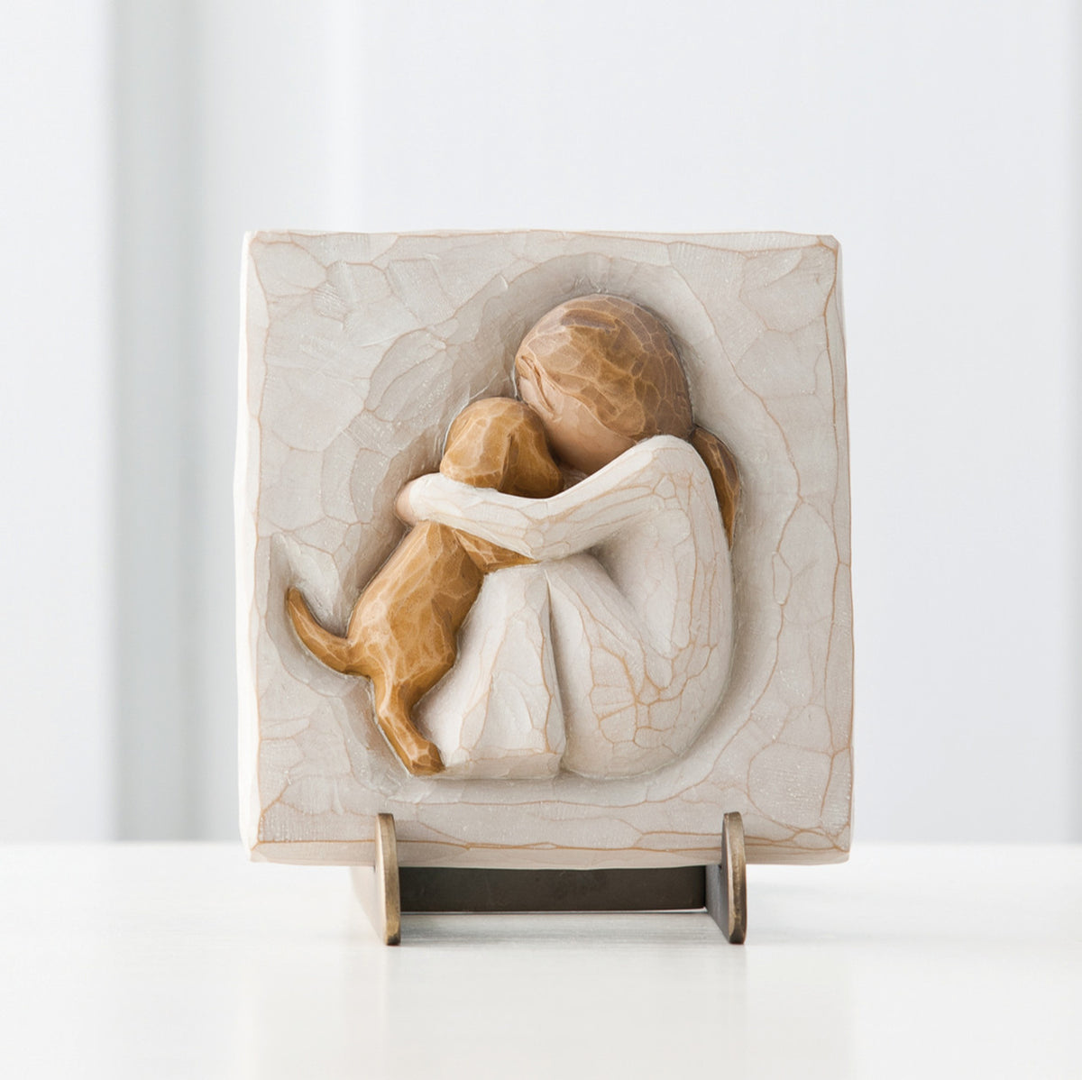 Close view of small cream square plaque on stand with carved in image of girl figurine hugging golden puppy