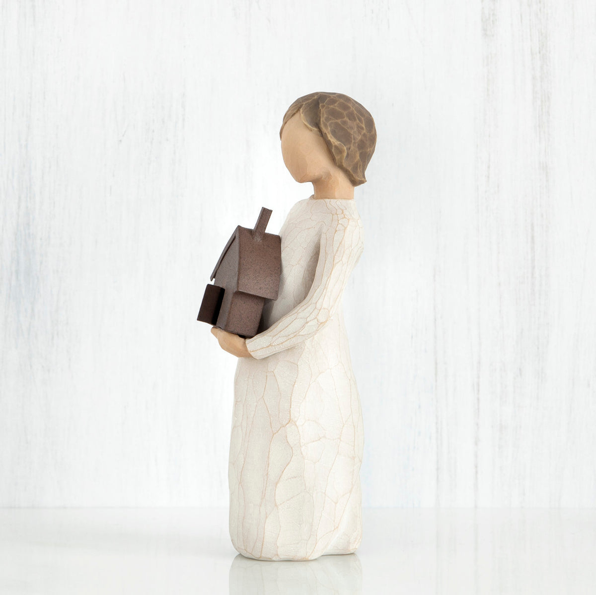 Side view of brunette figurine in white dress holding brown house figurine