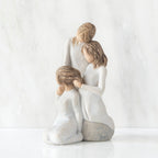 Left-facing view, figurine of three females in cream dresses: one standing with arm around kneeling female, and holding hand of seated female