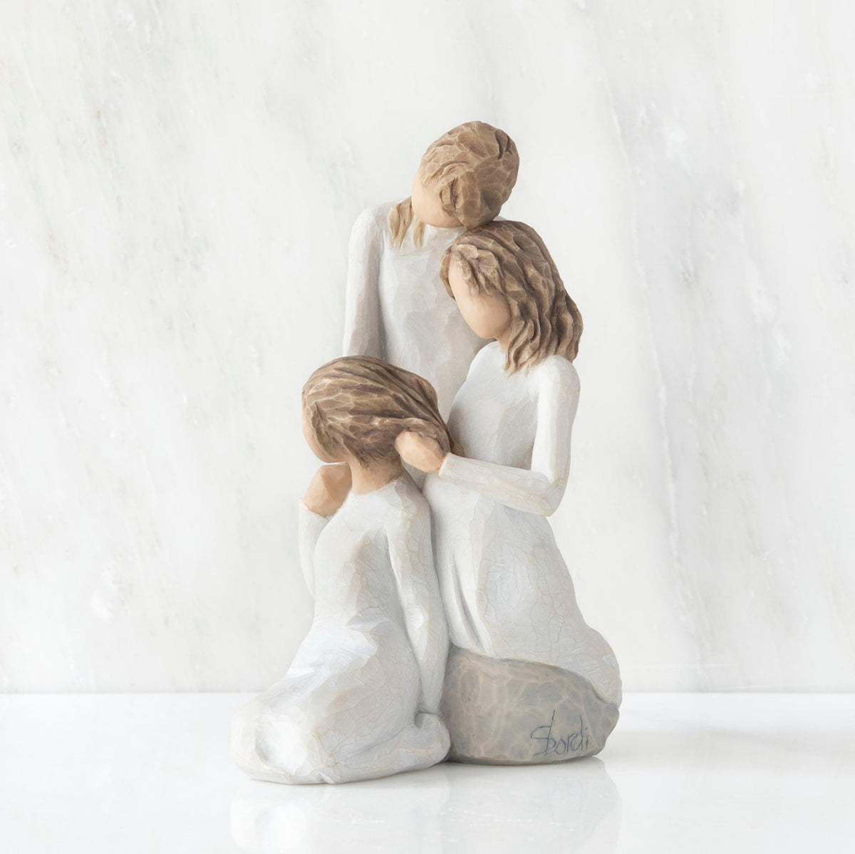 Left-facing view, figurine of three females in cream dresses: one standing with arm around kneeling female, and holding hand of seated female