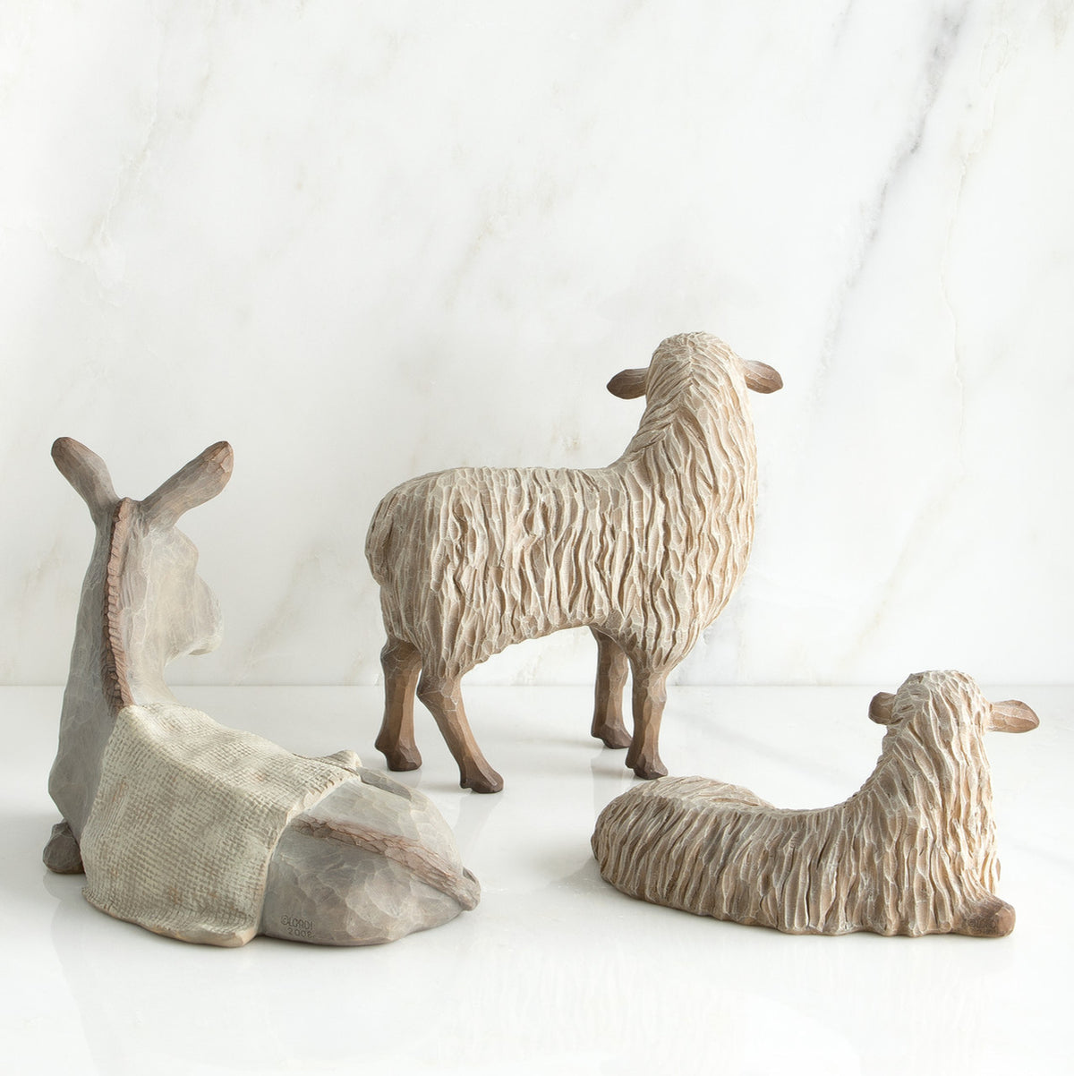 White donkey figurine laying down next to two white sheep figurines