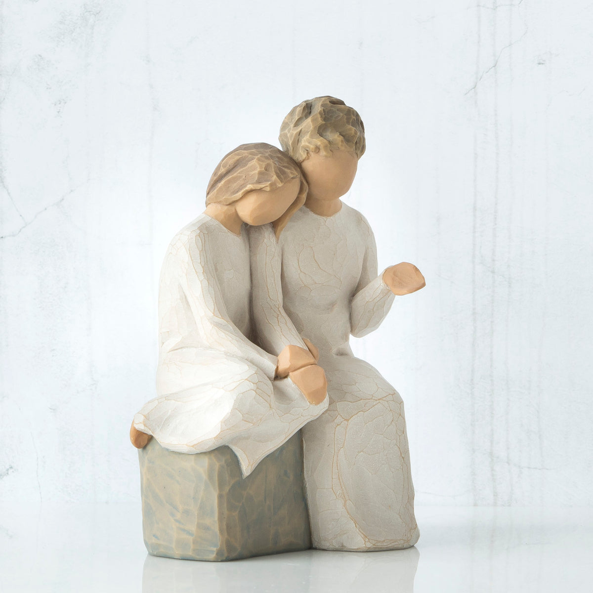 Front view - one girl figurine in white sitting on rock next to older girl figurine in white - holding hands