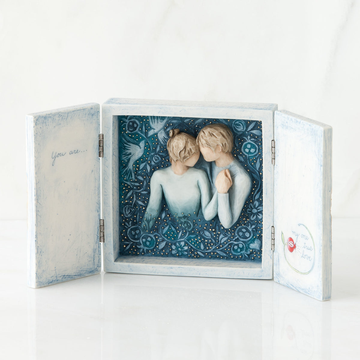 Open white/blue box with image of blue background and man and woman figurine in blue holding hands centered