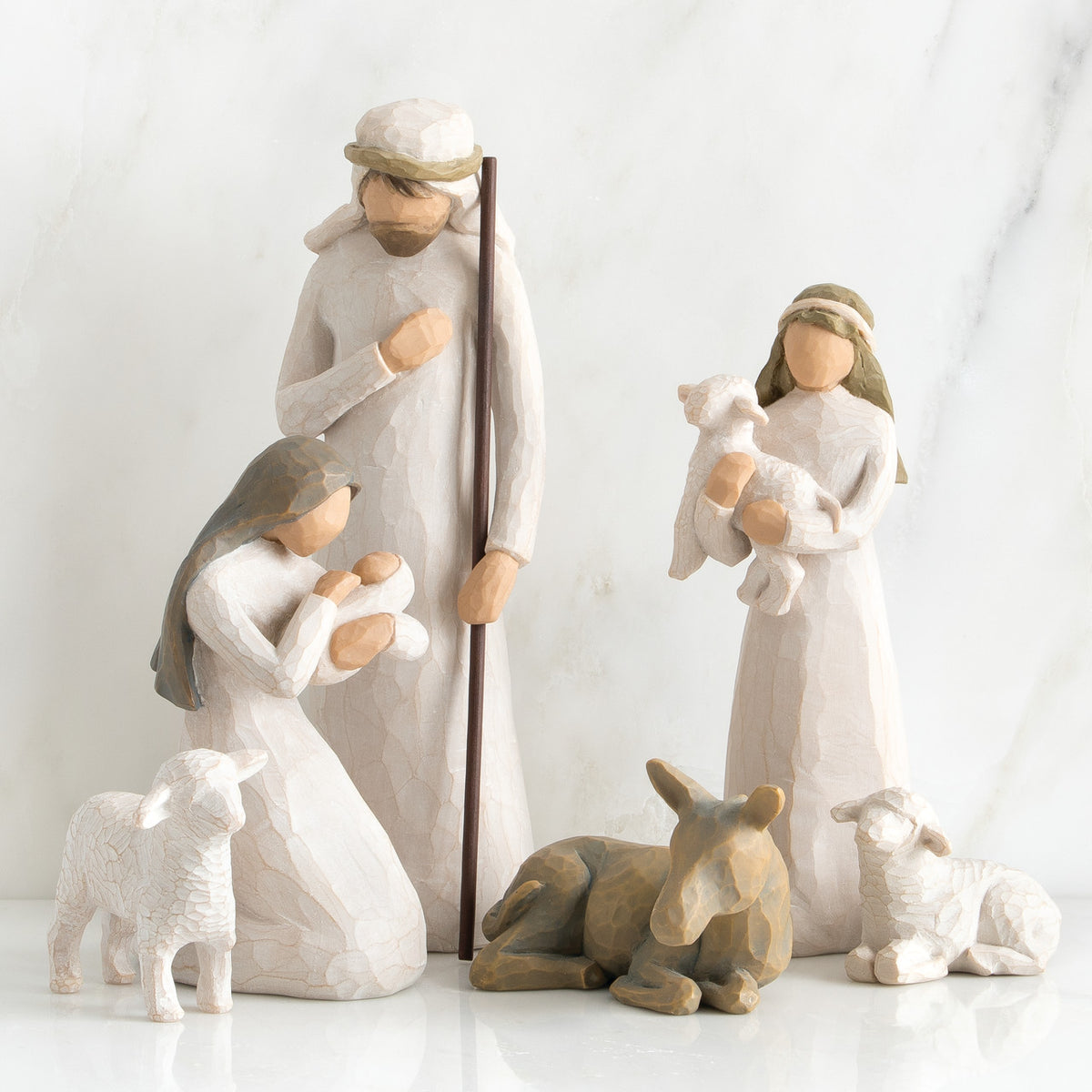 Set of two faceless woman figurines and one man figurine surrounded by laying donkey and three white sheep figurines