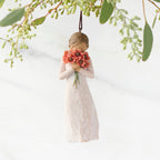 Figure in cream dress holding large bouquet of red-orange poppies up to face, ornament hook attached to head