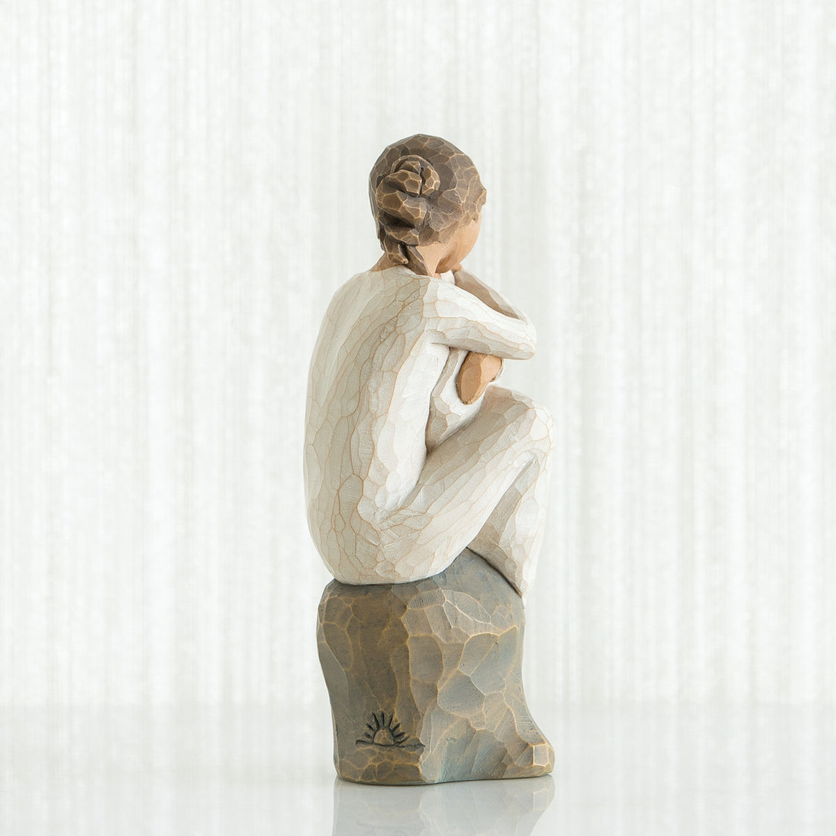 Back view of brunette girl figurine sitting down in white dress on rock