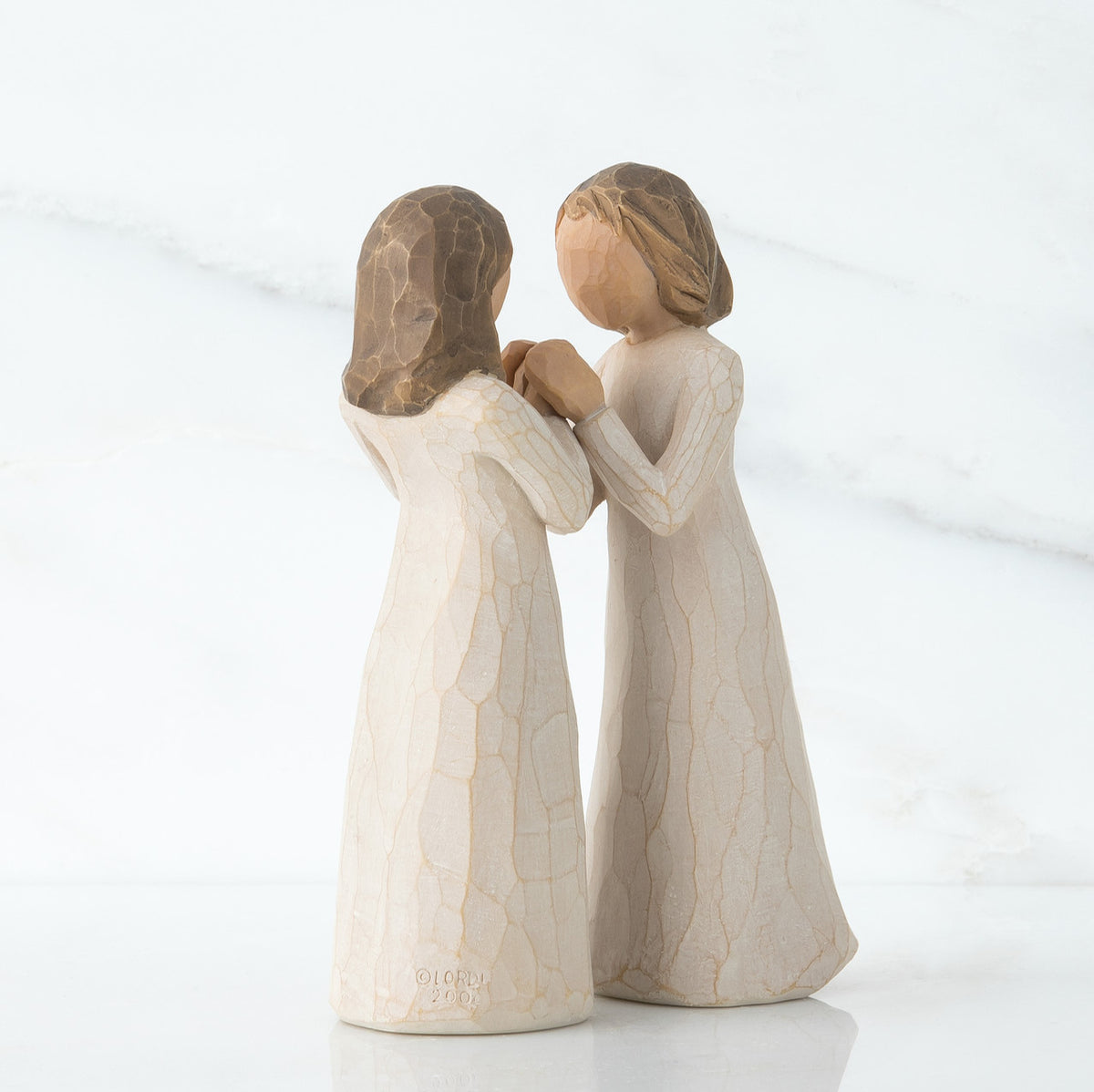 Close view of two brunette figurines in white dresses facing one another holding hands