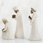 Three wiseman figurines in white dresses facing the side holding brown boxes
