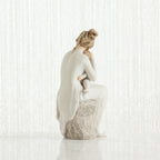 Woman figurine dressed in white sitting on rock holding baby - back view