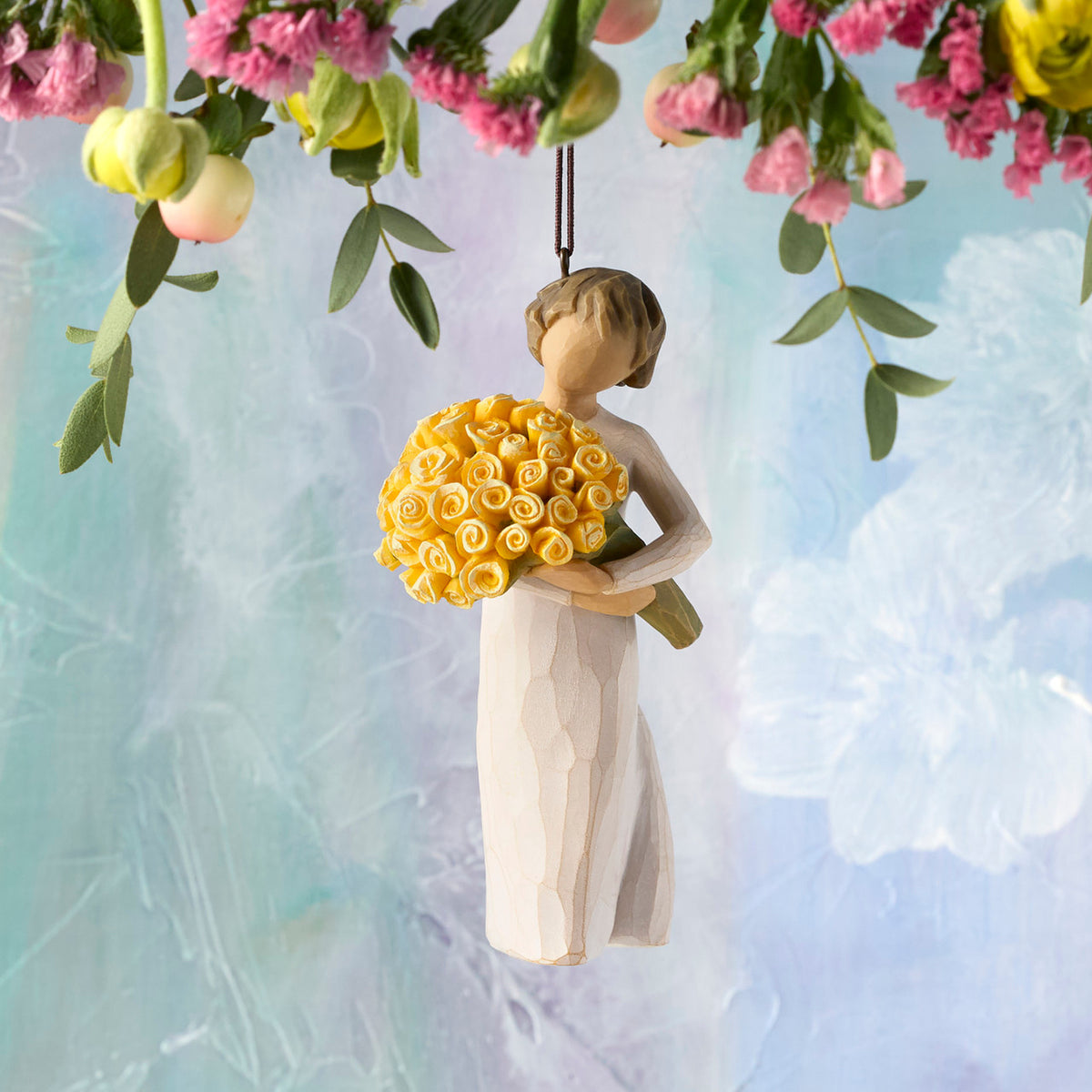 Willow Tree Good Cheer! Ornament, 4.5”h hand-painted resin figure in cream dress, holding bouquet of yellow roses, brown elastic cord, hanging in front of sky blue painting