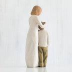 Blonde woman figurine in white dress with arms over boy figurine in white shirt and brown pants