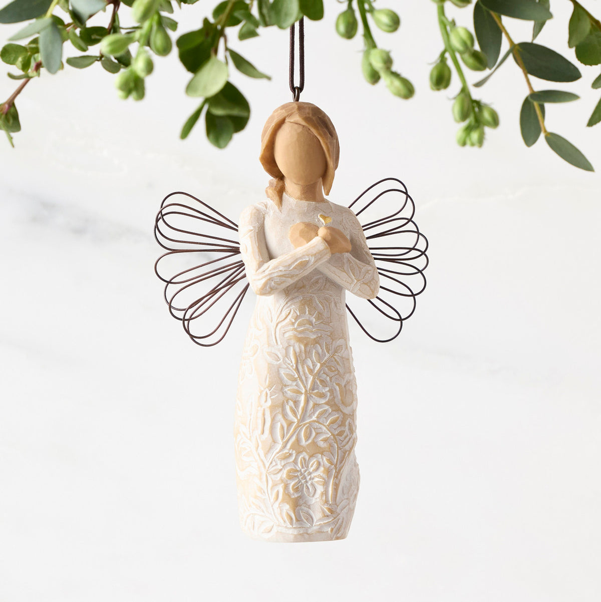 Front view of figure in cream dress carved with symbols of nature with wire wings, hands folded at chest around gold heart, ornament hook on head