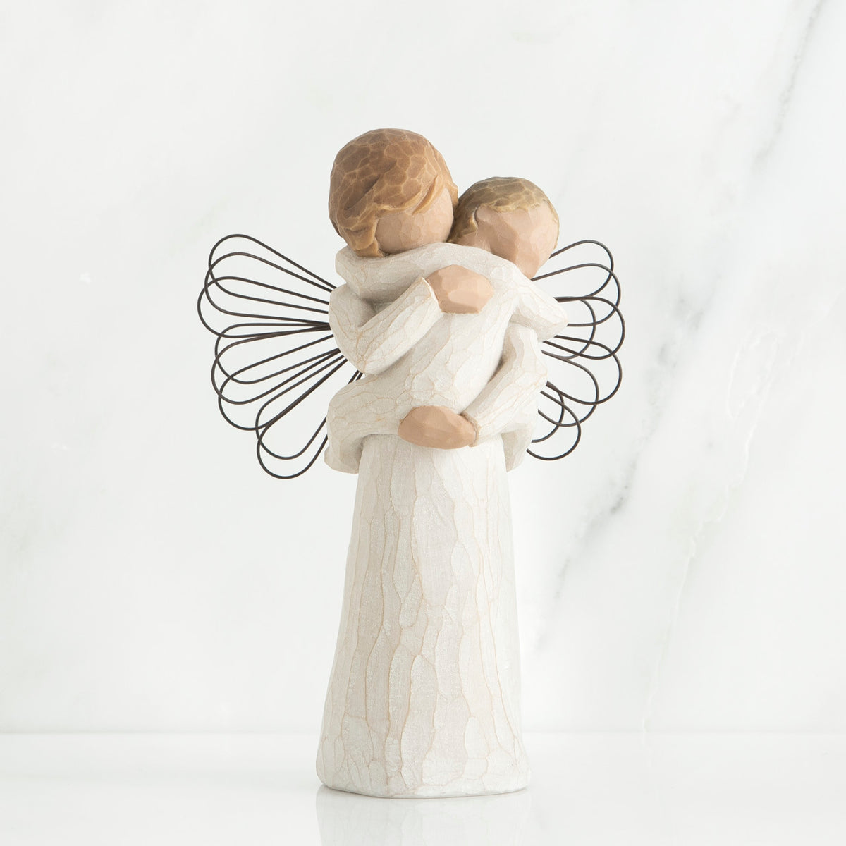 Young girl angel faceless figurine wearing white dress and has black wire wings, holding faceless baby in her arms