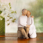 Willow Tree Anniversary, 6”h hand-painted resin figure of older couple sitting on bench holding hands, both in neutral clothing, on wood shelf with wildflowers