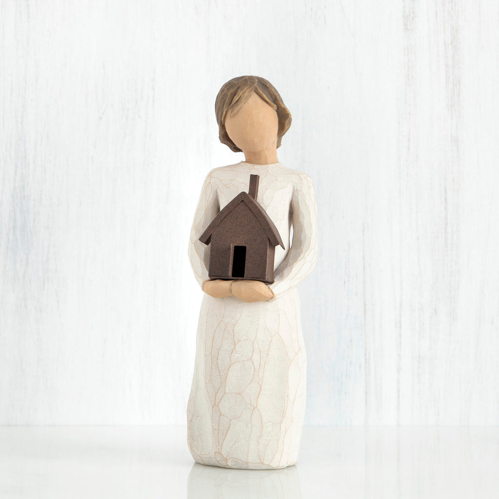 Faceless girl figurine facing forward wearing white dress, holding brown house figurine in her arms