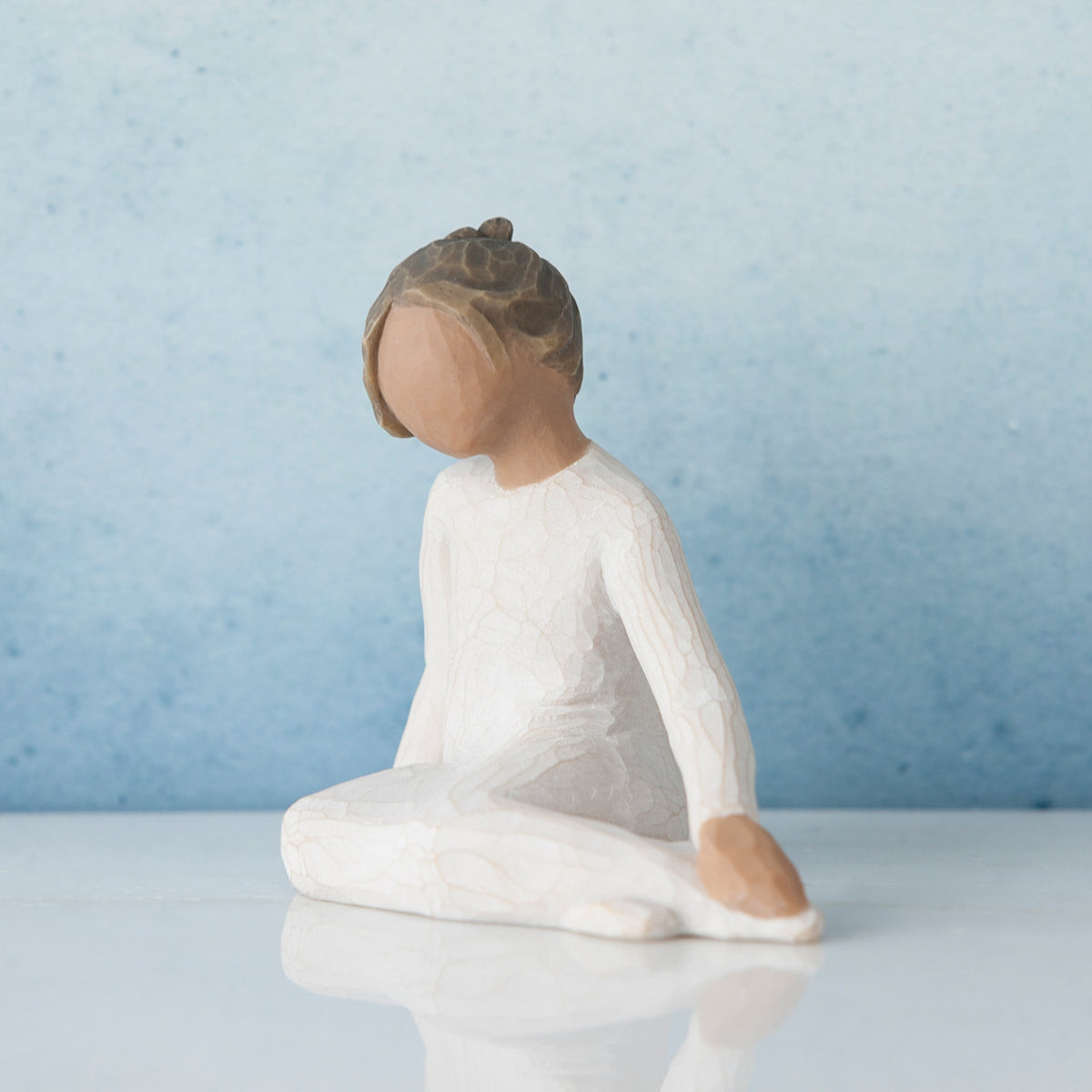 Small brunette girl figurine in white dress sitting down - blue background