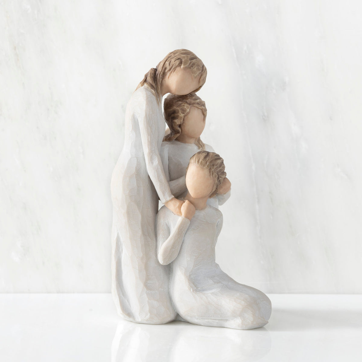 Right-facing view, figurine of three females in cream dresses: one standing with arm around kneeling female, and holding hand of seated female