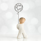 Front view of little boy with light brown hair holding a wire balloon behind his back. Text on balloon is wire