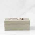Side view: Light gray rectangular wood box with hinged lid, carving on lid of female and child embracing in cream dresses