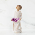 Front view of woman with tied back, curly, light brown hair holds up a portion of her dress's skirt as it is full of purple flowers