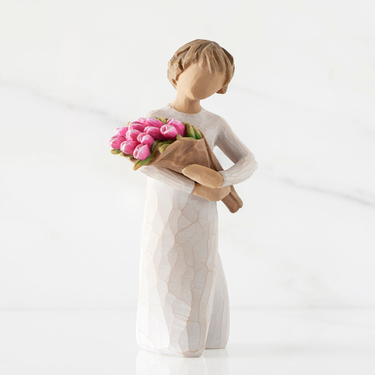 Right side of standing figure in cream dress holding bouquet of pink tulips