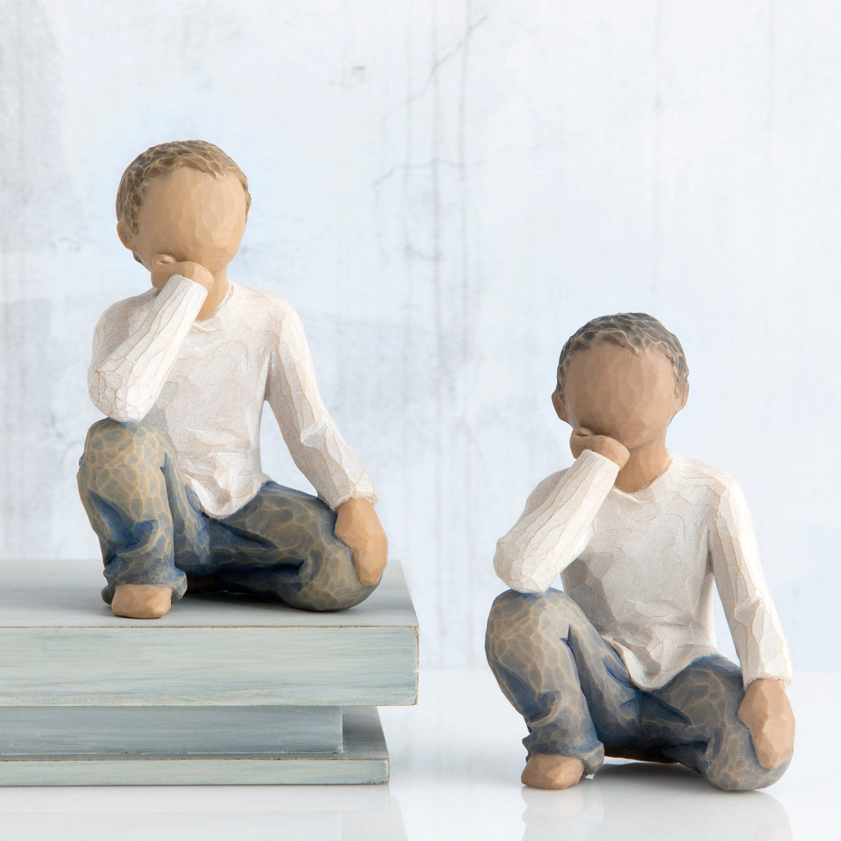 Set of two boy figurines in white shirts and blue jeans with their hands on their face