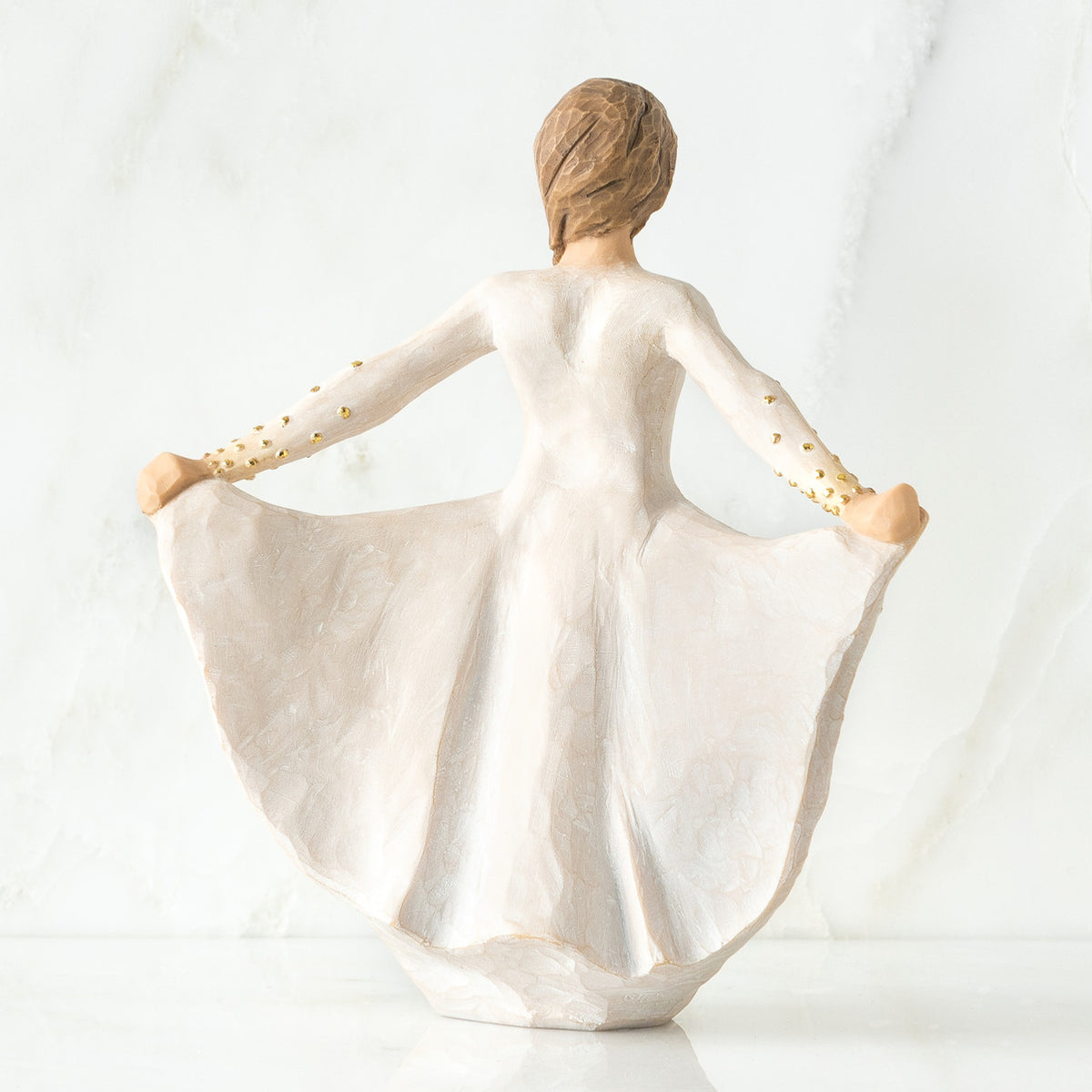 Back view of standing female figure in cream dress, holding out her skirt, which is carved with butterfly markings and dotted with gold