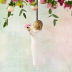 Willow Tree Thank You Ornament, 4”h hand-painted resin figure in cream dress, holding out bouquet of pink peonies, brown elastic cord, hanging in front of pastel painting