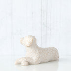 Figure of small white dog laying down with paws crossed in front, facing left