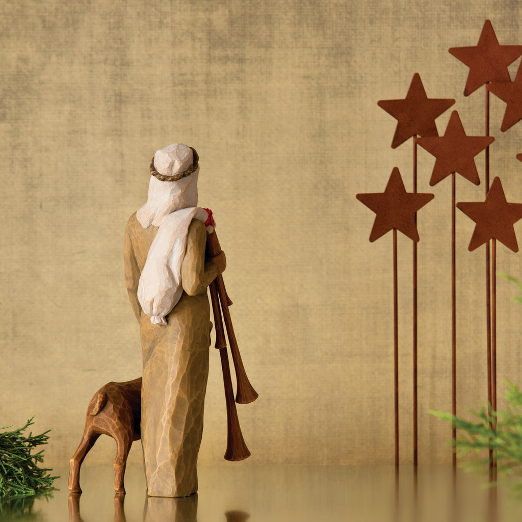 Back view of wiseman figurine in tan dress next to lamb - five red star stands to the right
