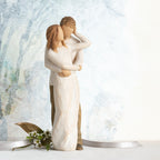 Willow Tree Together, 9”h hand-painted resin figure of couple, standing with arms around each other, dressed in neutral colors, both with lighter skin tones, in front of a blue painting