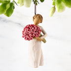 Front view of female figure with short brown hair holding large bouquet of pink roses, ornament loop affixed to top of head