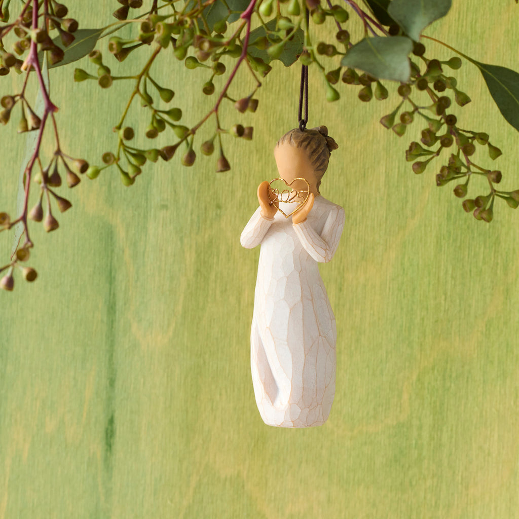 Willow Tree 2025 Ornament, 4”h hand-painted resin figure in cream dress, holding wire heart with 2025 inside, brown elastic cord, hanging in front of mossy green painting